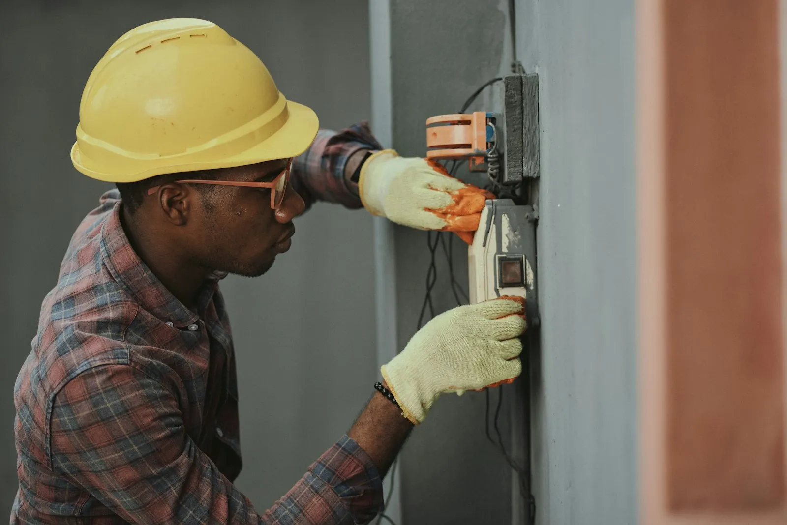 Un artisan électricien casqué intervient sur un boîtier électrique en chantier